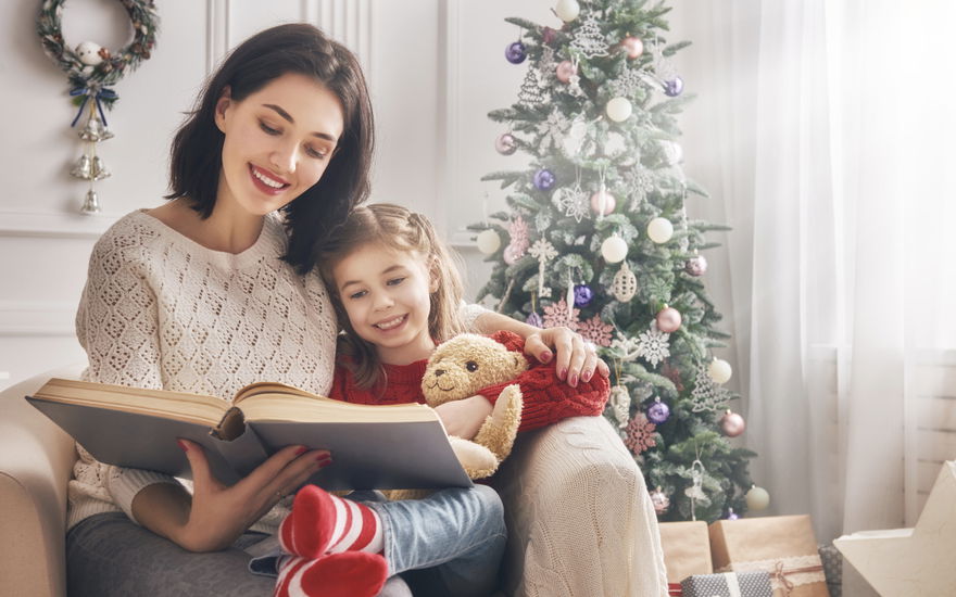 Mutter und Tochter lesen vor dem Weihnachtsbaum ein Buch zusammen