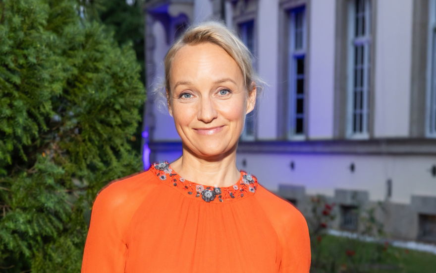 Eva Herzig trägt ein oranges Kleid