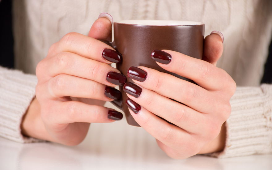 frau mit braunen nägeln hält tasse fest