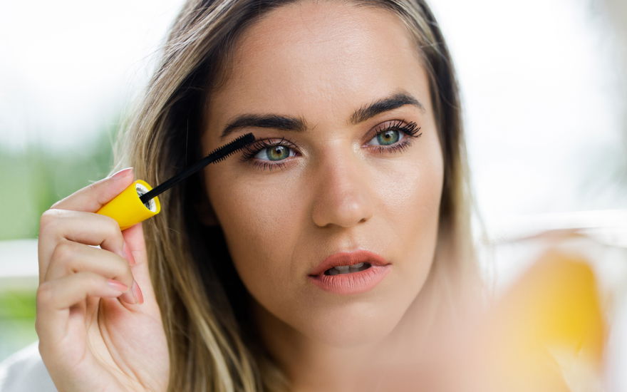 Frau trägt Mascara vor Spiegel auf