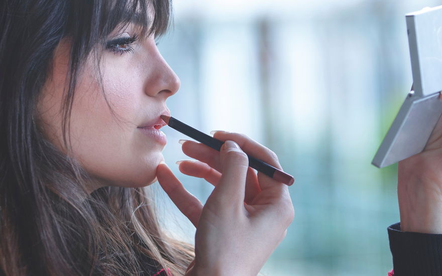 Frau mit dunklen Haaren malt Lippenkontur nach