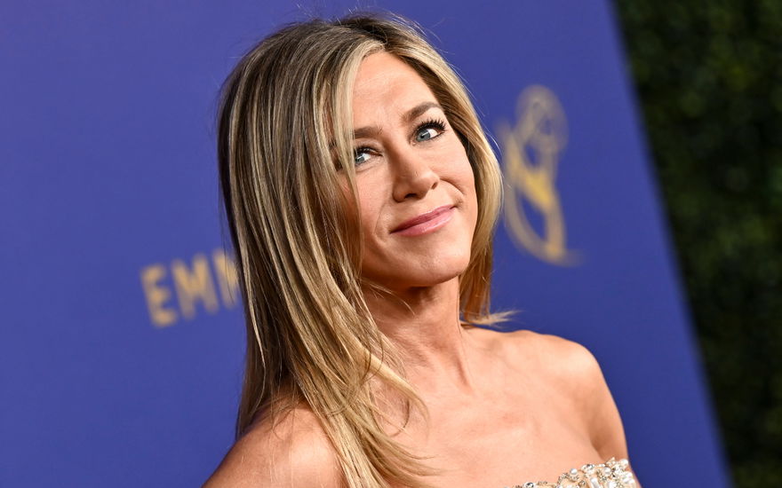Jennifer Aniston lächelt zur Seite vor lila Wand