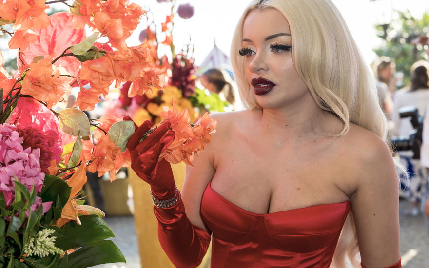 Katja Krasavice guckt ernst zur Seite, neben ihr Blumen