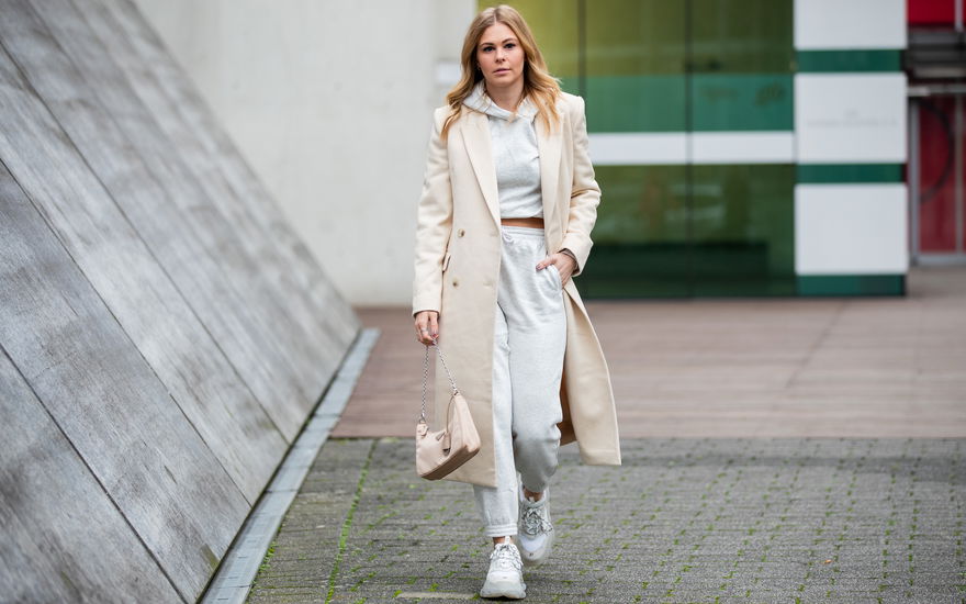Eine Frau trägt einen grauen Jogginganzug zu einem Mantel in Beige