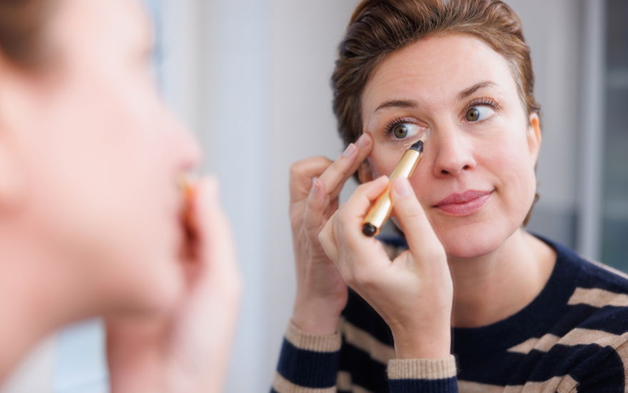 Frau trägt Concealer vor Spiegel auf