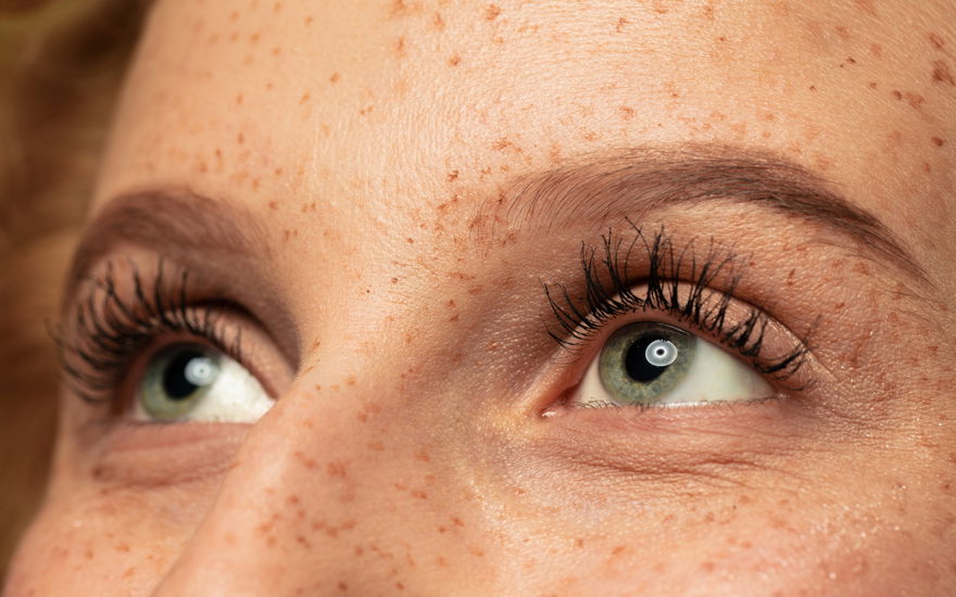 Frau mit grünen AUgen und Sommmersprossen zeigt lange Wimpern