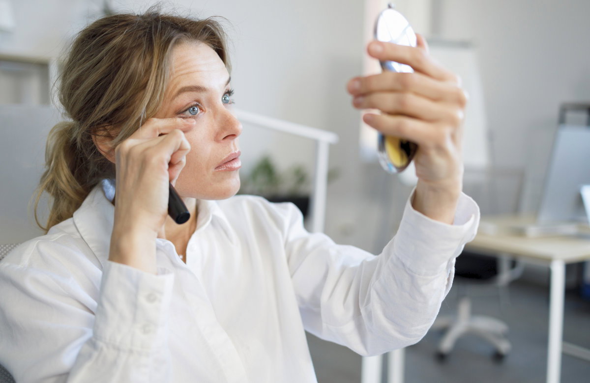 Frau mit Handspiegel schminkt wimpern