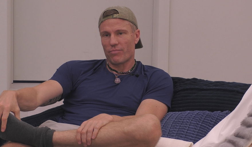 Christian Lell sitzt bei "Promi Big Brother" mit Cappy auf dem Sofa und grinst
