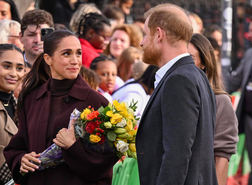 Herzogin Meghan schaut Prinz Harry in einer Menschenmenge an und hält einen Blumenstrauß in ihren Händen