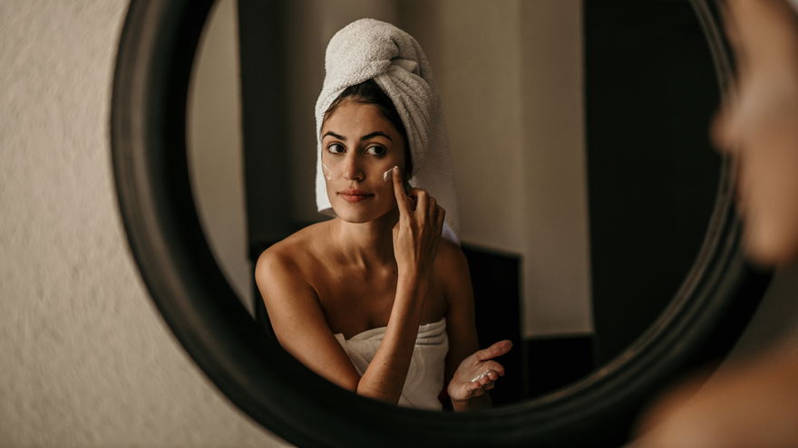 Frau mit Handtuch-Turban cremt sich ein