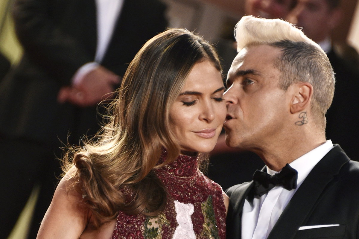 Robbie Williams küsst seine Ehefrau Ayda Field auf die Wange.