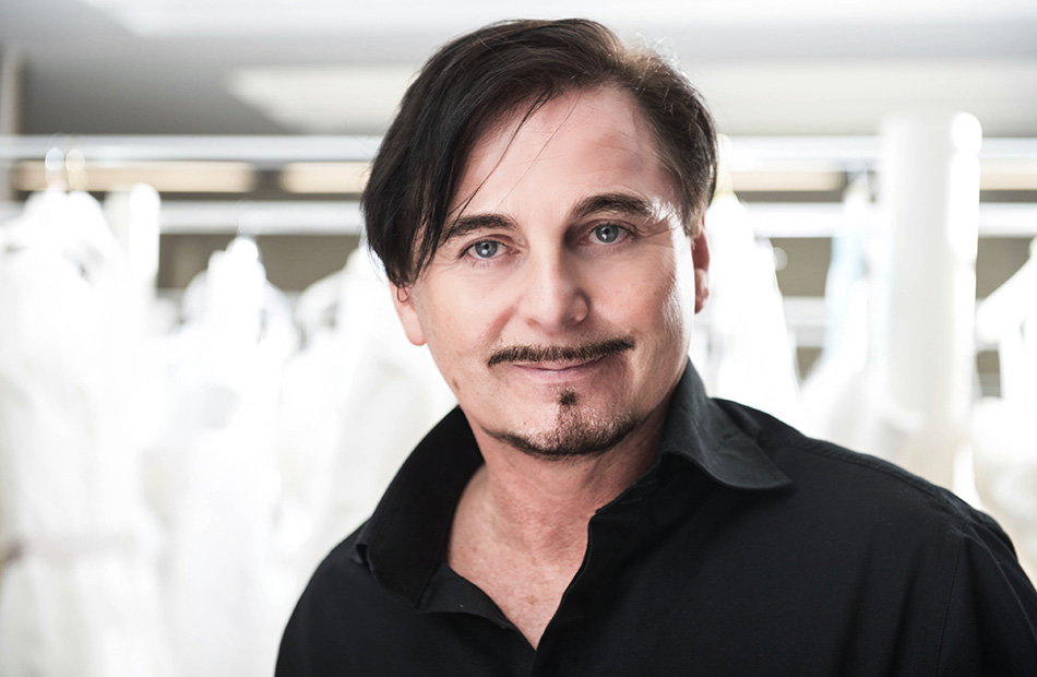 Uwe Herrmann posiert vor Brautkleidern und lächelt in die Kamera