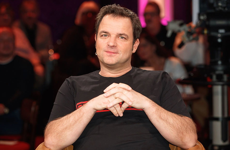 Martin Rütter sitzt mit verschränkten Armen auf einem Stuhl in einer Talkshow
