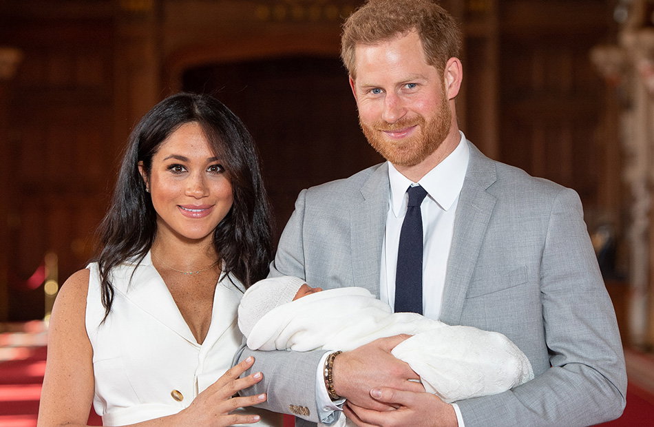 Harry und Meghan lächeln in die Kamera während Harry Archie hält.