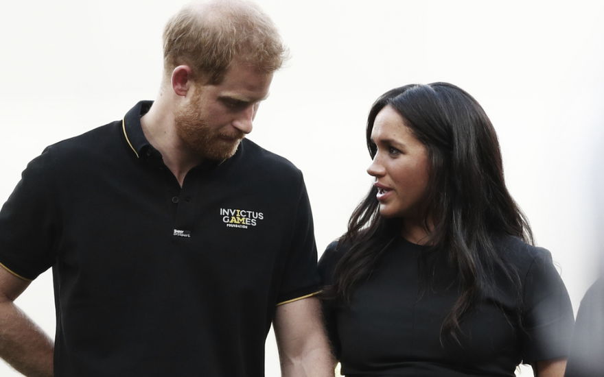 Prinz Harry sieht zu Boden, Herzogin Meghan sieht in fordernd an