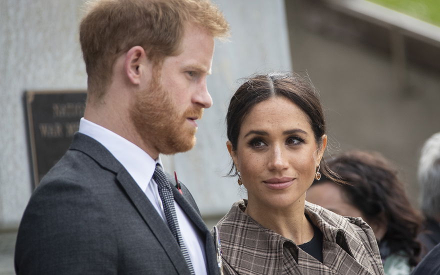 Prinz Harry schaut ernst, Ehefrau Meghan sieht ihn fragend an