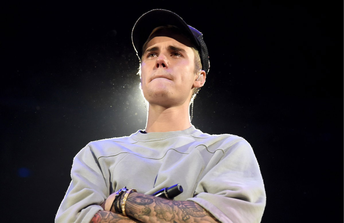 Justin Bieber steht mit verschränkten Armen und zusammengepressten Lippen da.