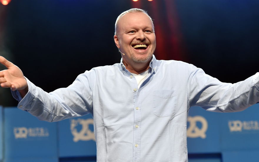 Stefan Raab lacht auf der Bühne und hält die Arme auf
