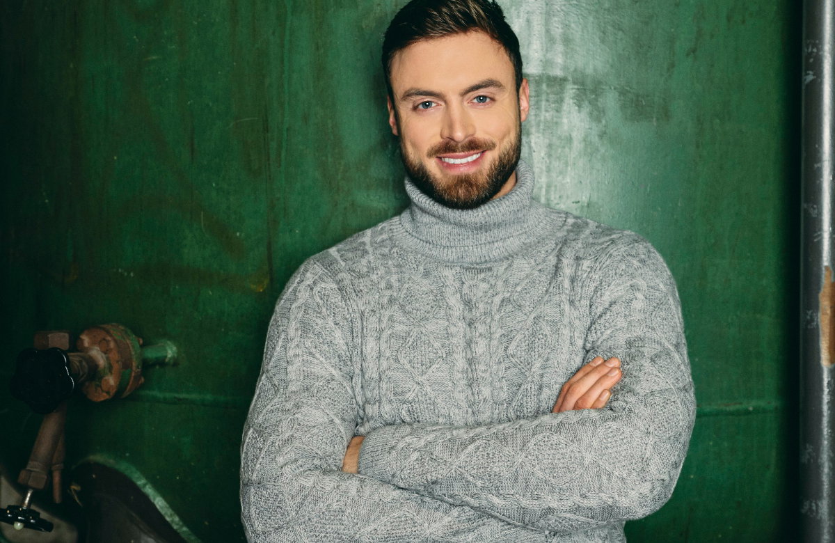 Niko Griesert steht lächelnd mit verschränkten Armen vor einer grünen Wand.