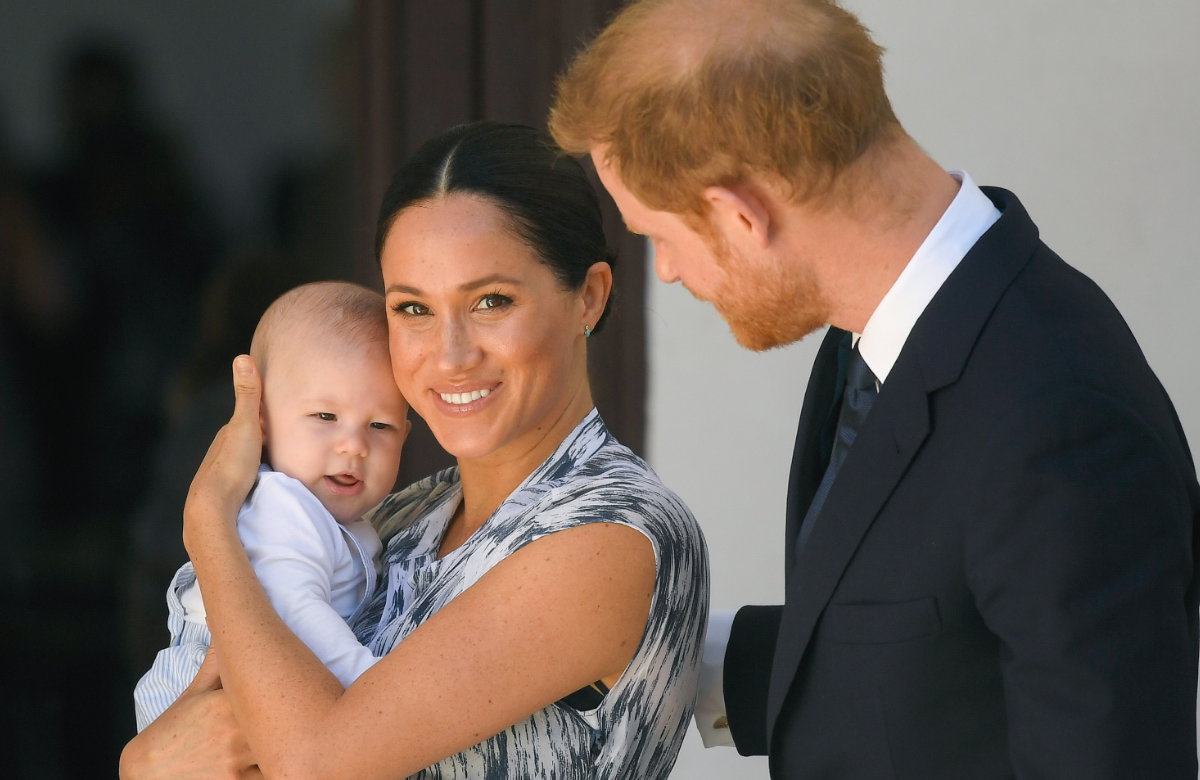 Meghan lächelt in die Kamera und hält Archie im Arm.