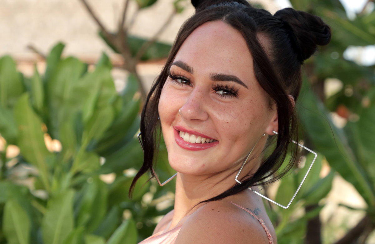 Alessa Herren strahlt, grüne Pflanzen im Hintergrund