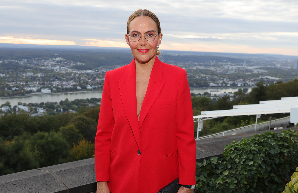 Natascha Ochsenknecht steht in einem roten Blazer oberhalb eines Flusses