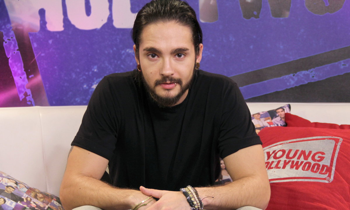 Tom Kaulitz sitzt auf Sofa und guckt in die Kamera